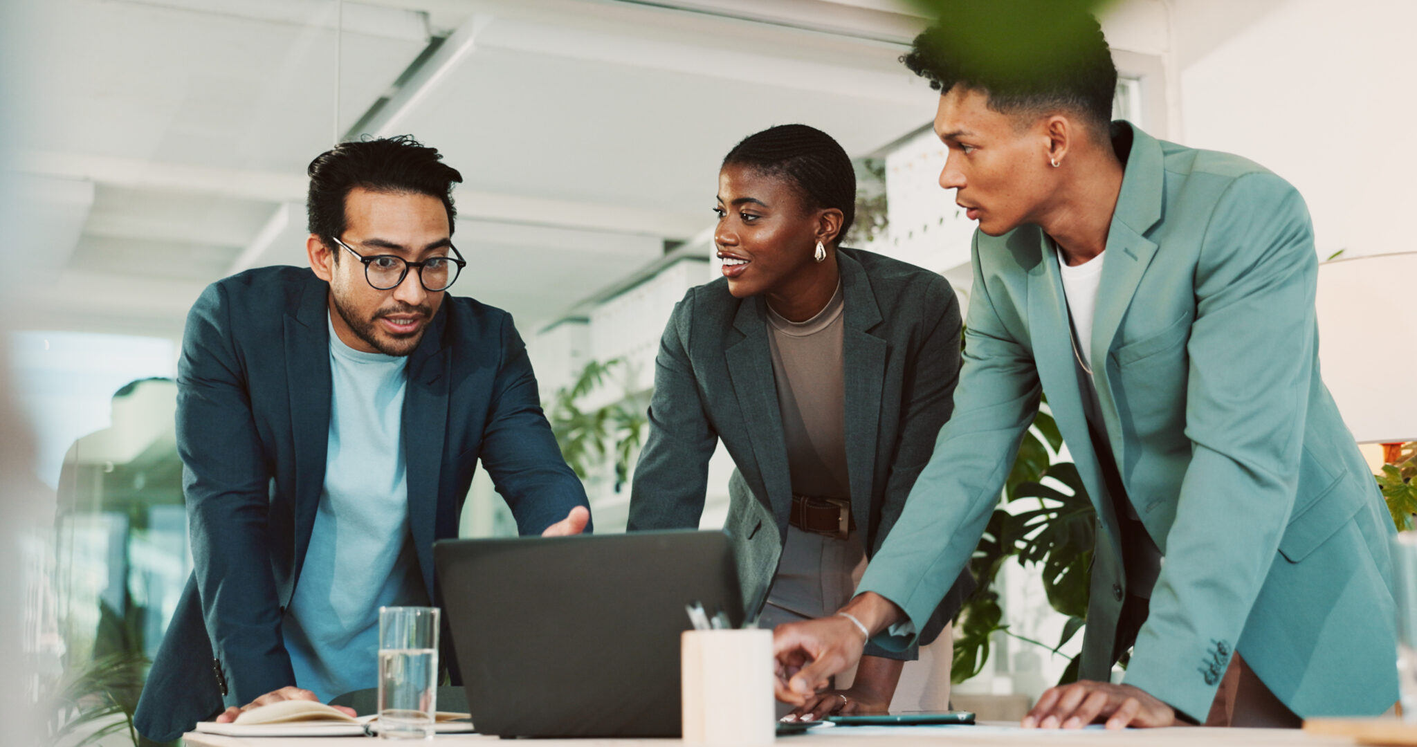 Three business professionals collaborating in a modern office, engaged in a discussion over a laptop – teamwork, strategy, and innovation in a corporate setting.